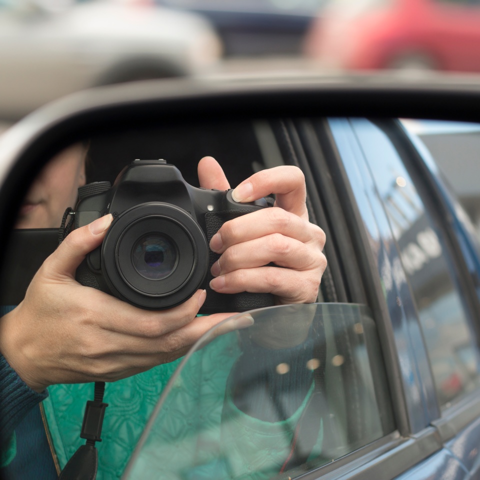 Hidden photographing. Reflection in car mirror of woman with camera. Paparazzi concept