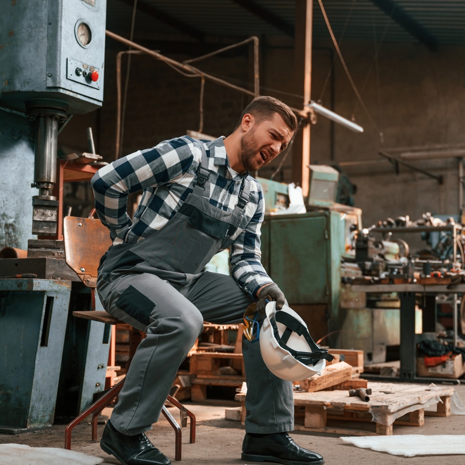 Felling bad. Back is hurting. Factory male worker in uniform is indoors.