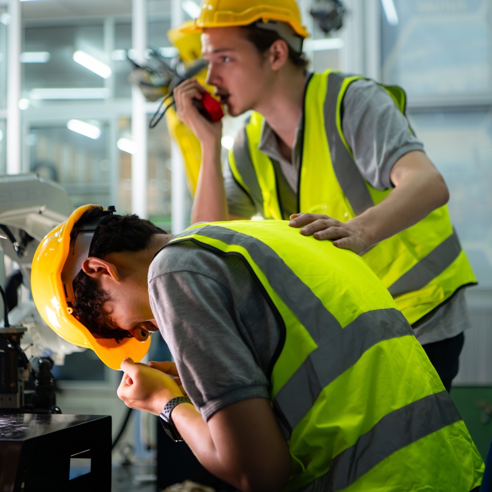 A technician suffers a hand accident while working with a robot arm in a factory with co-workers providing assistance