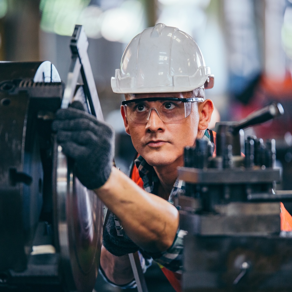 Male engineer metalworker industrial experienced operator technician worker in safety hard helmet working on lathe machine, professional man in industry technology manufacturing factory workshop